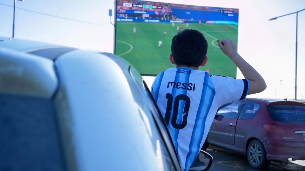 Vecinos de Río Grande reunidos frente a una pantalla gigante en el Parque de los 100 Años con banderas argentinas