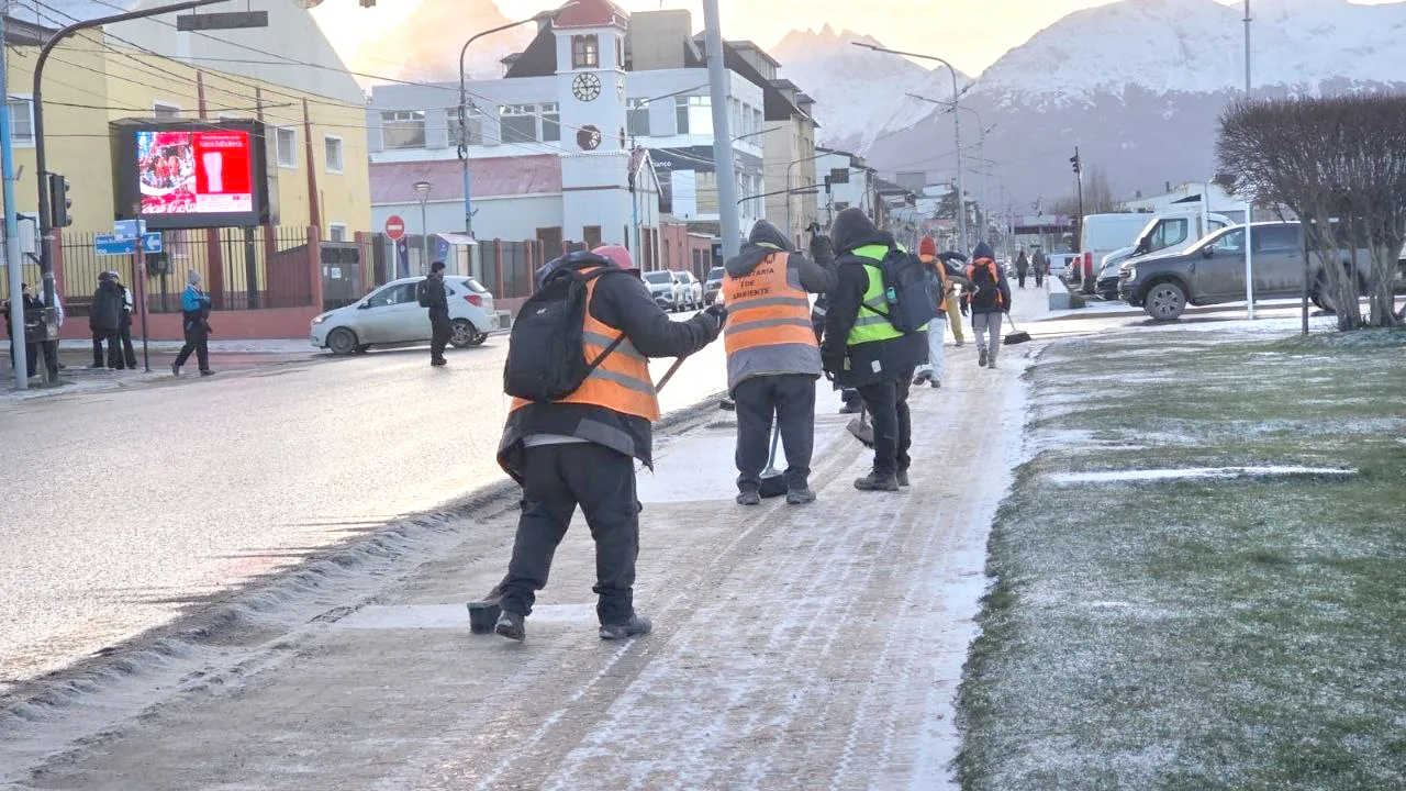 Trabajadores municipales quitando nieve de una vereda en Ushuaia con palas y sal