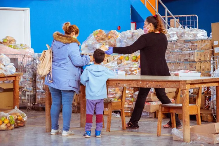 Persona recibiendo módulo alimentario en Tolhuin, con bolsa de alimentos y carteles del programa Bienestar
