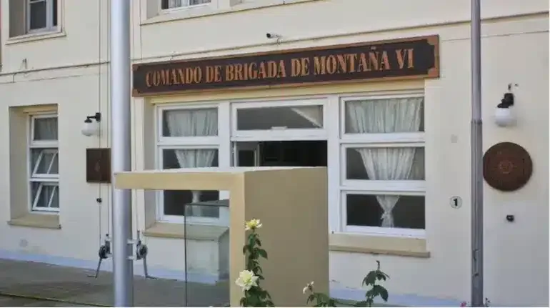 Edificio principal de la Brigada de Montaña VI de Neuquén con postes de luz y cables en primer plano