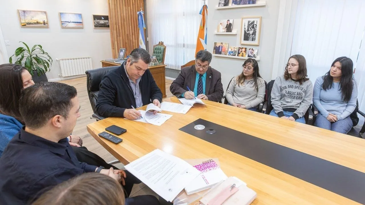Autoridades de Río Grande y UTN firmando convenio de pasantías en mesa con banderas de fondo