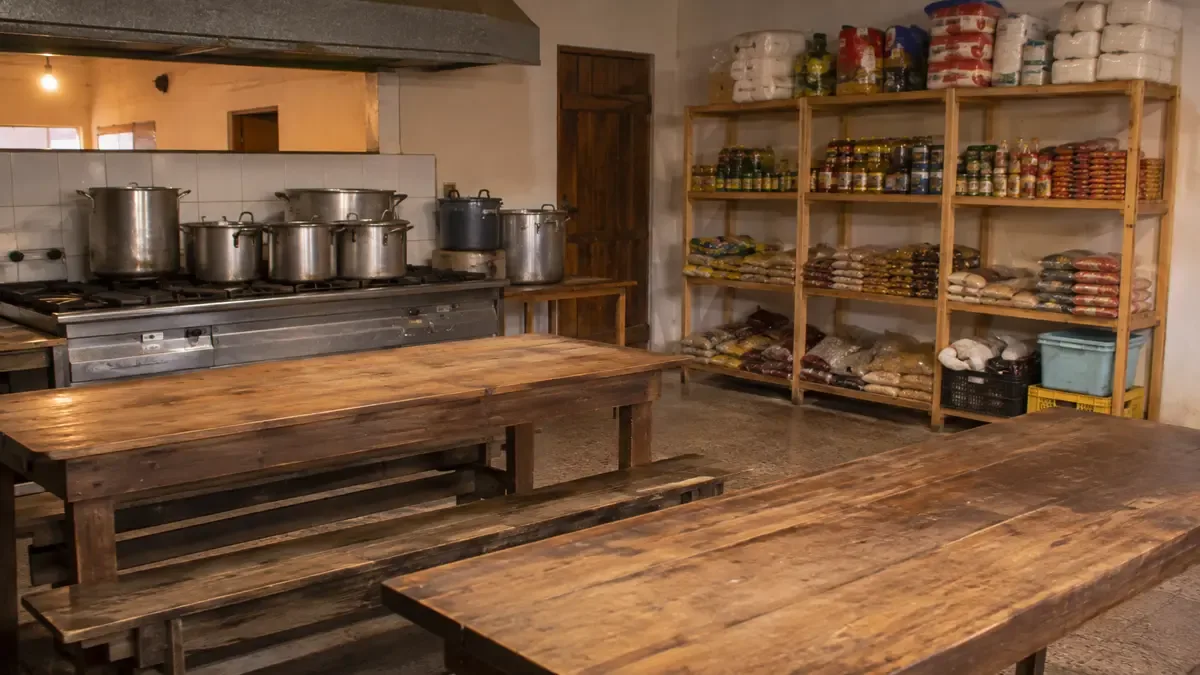 Comedor comunitario de barrio con mesas vacías y ollas sobre la cocina
