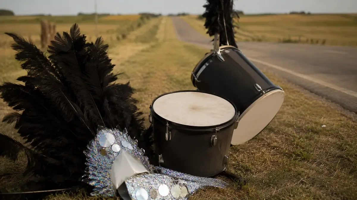 Plumas, lentejuelas y tambores sin insignias en una ruta entrerriana entre campos, vista en tres cuartos, profundidad de campo suave